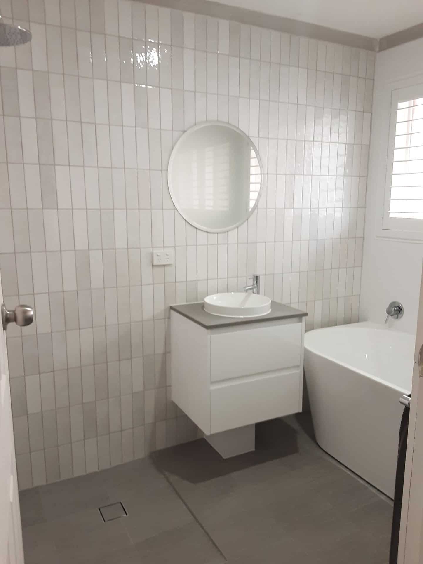 Vertical white subway tile ensuite with a freestanding bath and round mirror