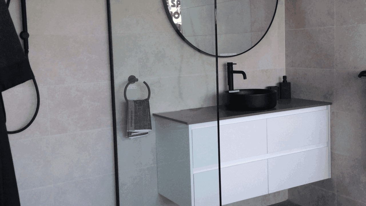 Grey stone-look ensuite in the BRW showroom with black tapware, a round mirror and a wall-hung vanity